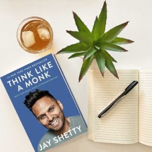 Think like a monk book by Jay Shetty shown with a plant, a journal, a pen and a glass of iced tea