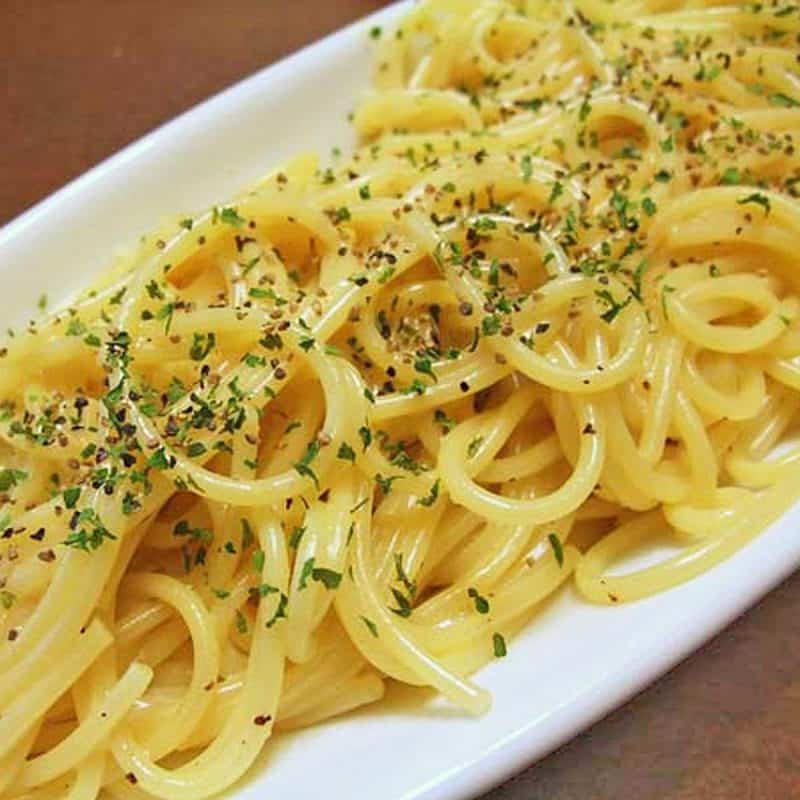 A white serving dish filled with pasta topped with cheese sauce and parsley.