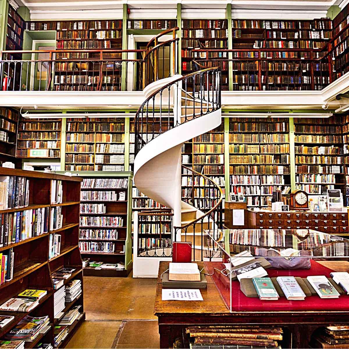 A large library filled with shelves of books, with a two-story spiral staircase in the center of the room.