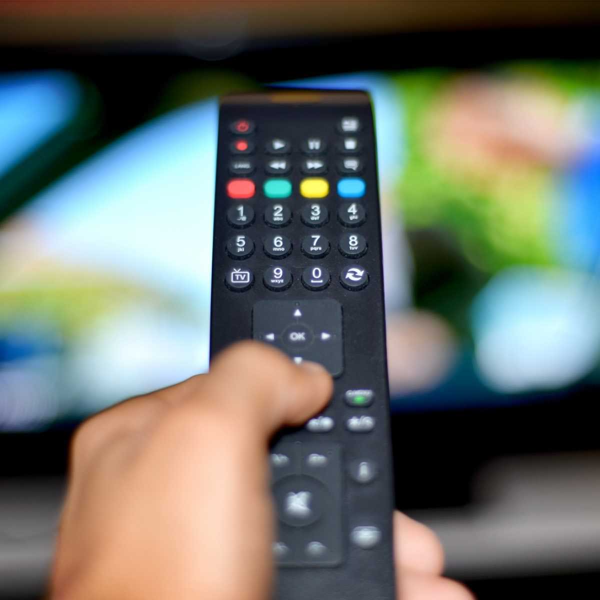 A man's hand holding a remote control aimed at a tv
